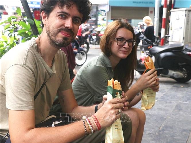 Du khách thưởng thức bánh mì truyền thống của Hà Nội trên phố Hàng Bông. 