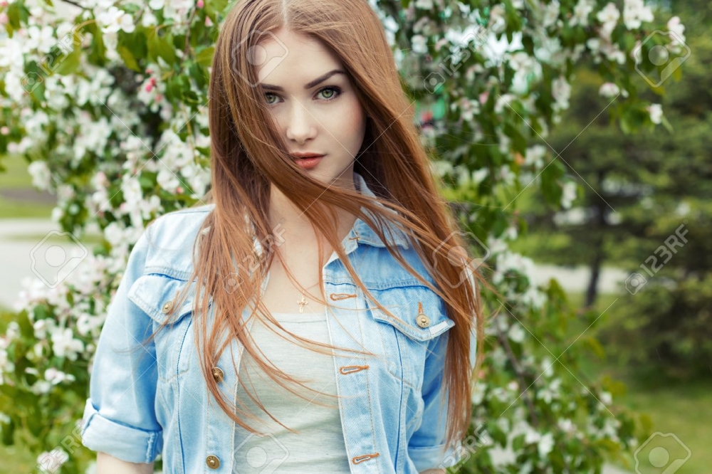 0219 41733034 beautiful sexy cute sweet girl with long red hair and green eyes in a denim jacket near a flowering